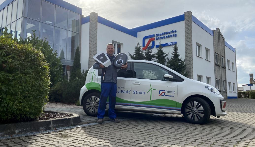 Ein Mitarbeiter steht vor einem Auto und hält technische Komponenten hoch